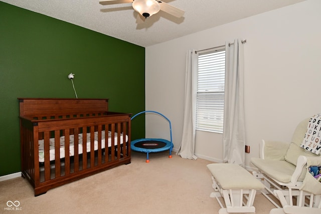 bedroom with carpet, a ceiling fan, a textured ceiling, a crib, and baseboards