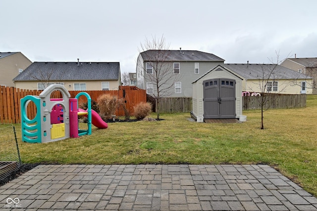 view of jungle gym featuring an outbuilding, a fenced backyard, a lawn, and a storage unit