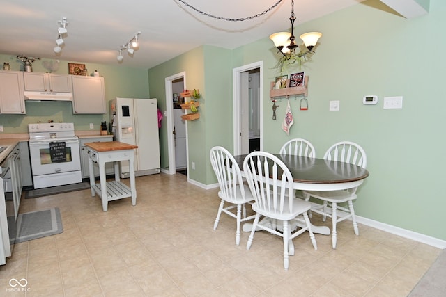 kitchen with baseboards, hanging light fixtures, white appliances, and under cabinet range hood