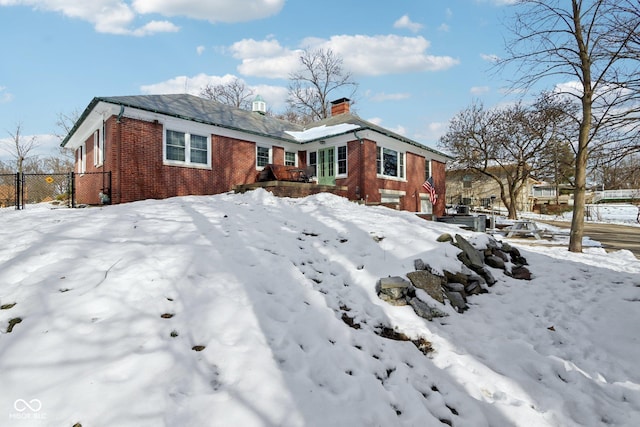 snow covered property with a garage, a chimney, fence, and brick siding