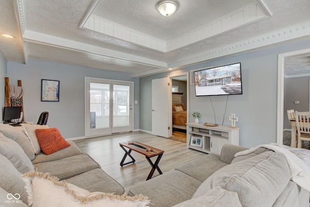 living area with a textured ceiling, a tray ceiling, light wood finished floors, and baseboards