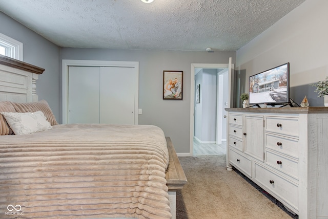 bedroom with a closet, baseboards, a textured ceiling, and light colored carpet