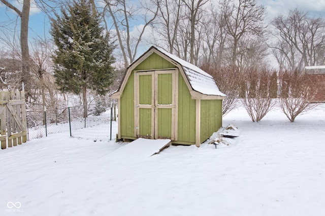 snow covered structure featuring a storage unit and fence