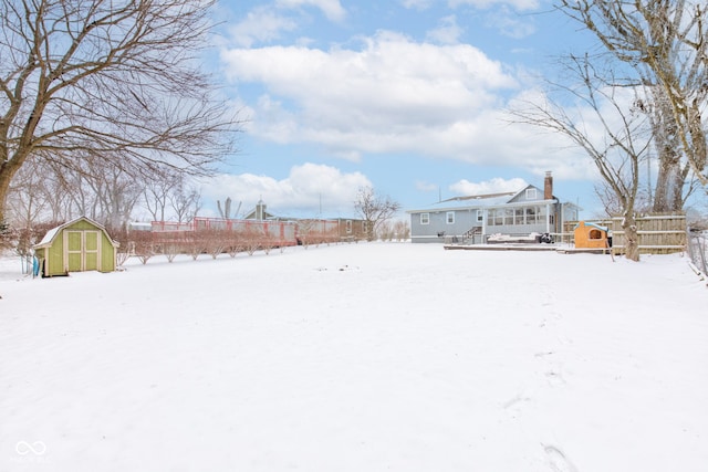 yard layered in snow with fence, a storage unit, and an outdoor structure