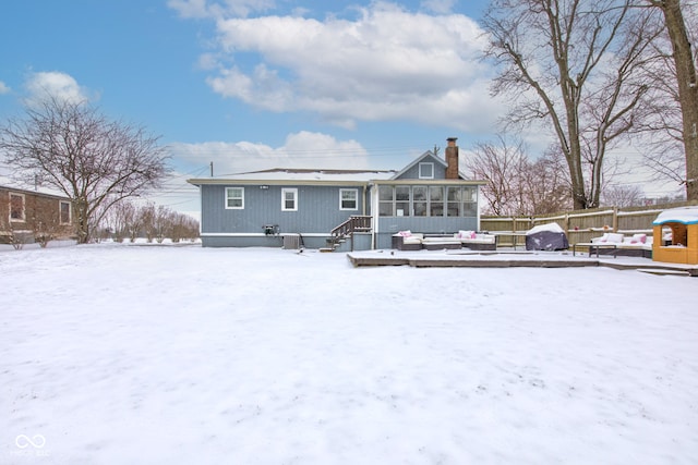 snow covered rear of property featuring a chimney and a sunroom