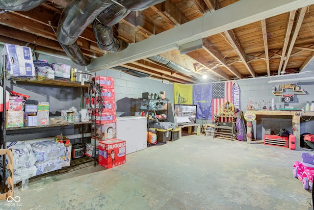 unfinished basement with a workshop area, concrete block wall, and refrigerator