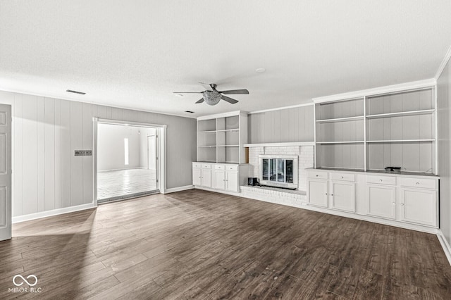 unfurnished living room with ornamental molding, dark wood-style flooring, a brick fireplace, and visible vents