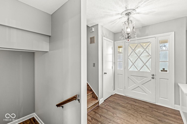 entryway with visible vents, a notable chandelier, baseboards, and wood finished floors