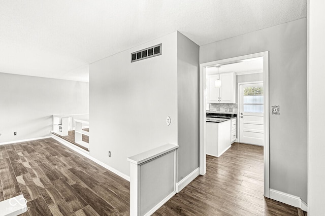 corridor featuring dark wood-style floors, visible vents, a textured ceiling, and baseboards