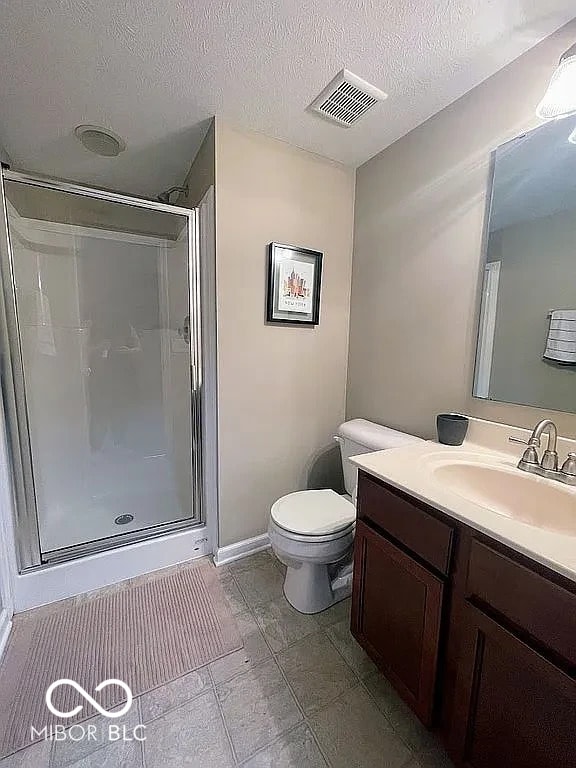 full bath with visible vents, toilet, a textured ceiling, a shower stall, and vanity