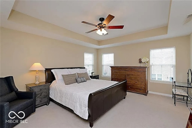 bedroom with a ceiling fan, a raised ceiling, light colored carpet, and baseboards