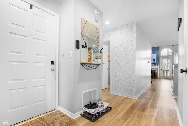 entrance foyer with wallpapered walls, wood finished floors, visible vents, and baseboards