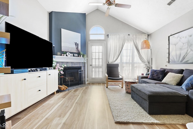 living area with high vaulted ceiling, a fireplace, a ceiling fan, and light wood-style floors