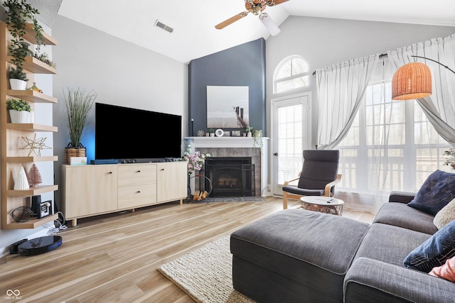 living room with high vaulted ceiling, a tile fireplace, visible vents, a ceiling fan, and light wood-type flooring