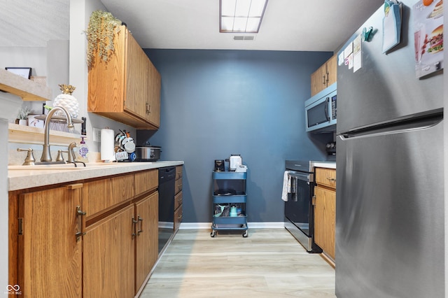 kitchen featuring light countertops, appliances with stainless steel finishes, a sink, and brown cabinets