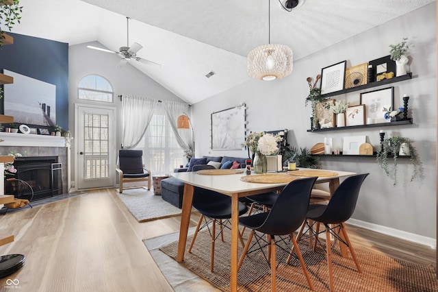 dining area with visible vents, a tile fireplace, ceiling fan, wood finished floors, and high vaulted ceiling