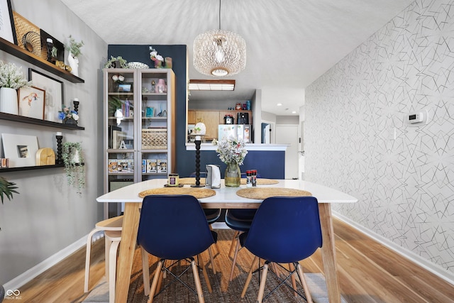 dining room with an accent wall, baseboards, light wood finished floors, and wallpapered walls