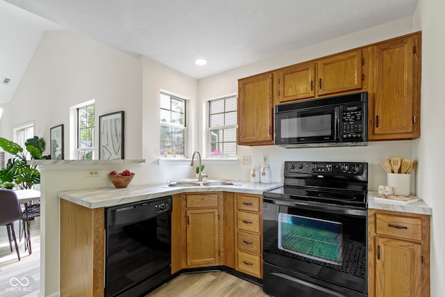 kitchen with black appliances, a sink, light wood-style flooring, brown cabinets, and light countertops