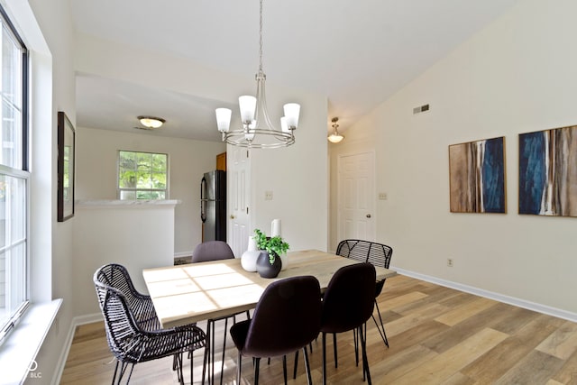 dining area featuring a chandelier, light wood-style flooring, baseboards, and vaulted ceiling