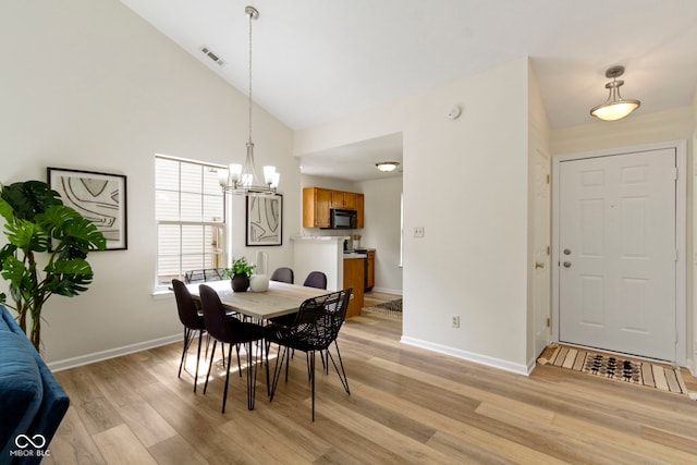 dining area with a chandelier, high vaulted ceiling, light wood-style flooring, and baseboards