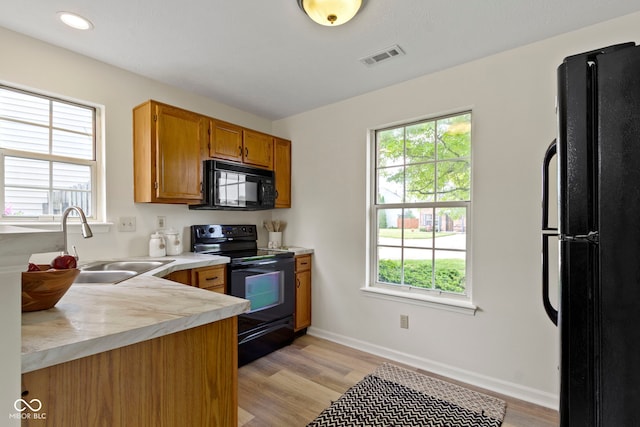kitchen with black appliances, a sink, light countertops, brown cabinets, and plenty of natural light