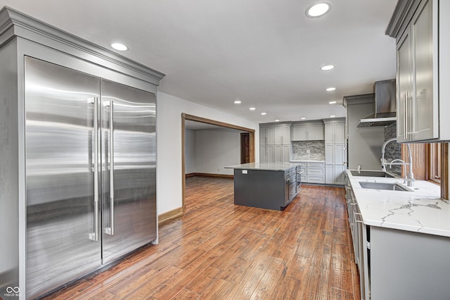 kitchen featuring wall chimney range hood, gray cabinetry, dark wood-style floors, and built in fridge