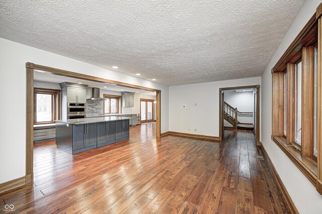690 N 600 W, Lebanon, IN 46052 - kitchen featuring wall chimney exhaust hood, gray cabinets, stainless steel double oven, a kitchen island, and hardwood / wood-style floors