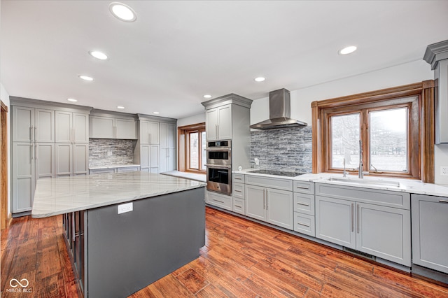 kitchen with double oven, black electric cooktop, gray cabinetry, a center island, and wall chimney exhaust hood