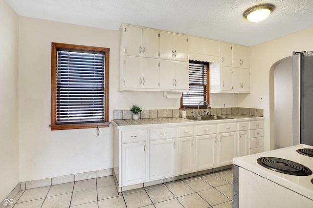 kitchen with arched walkways, tile countertops, white electric range, freestanding refrigerator, and a sink