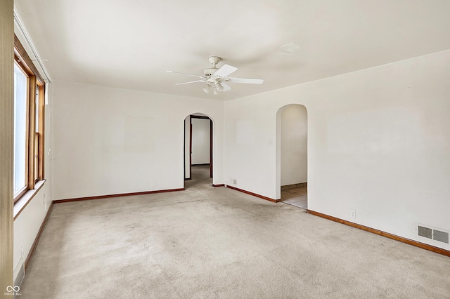 unfurnished room featuring arched walkways, light colored carpet, a ceiling fan, baseboards, and visible vents