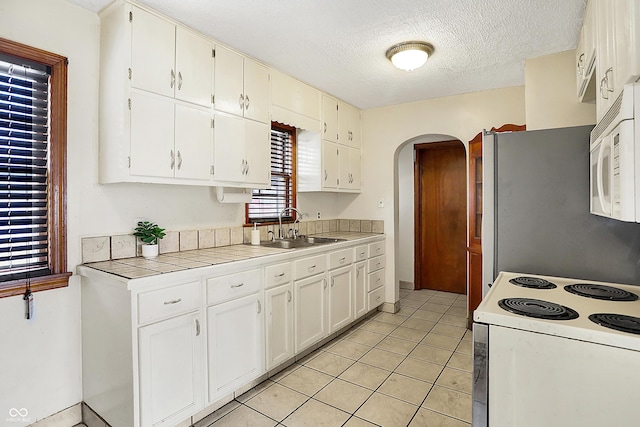 kitchen featuring white appliances, tile counters, arched walkways, a textured ceiling, and a sink