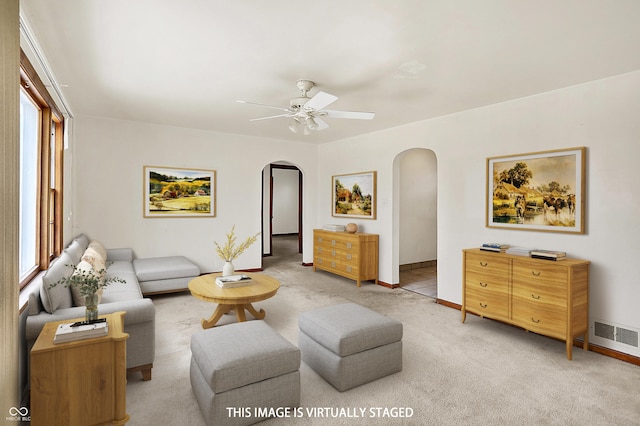 living area with arched walkways, ceiling fan, light colored carpet, visible vents, and baseboards