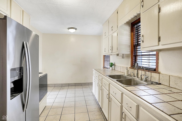 kitchen featuring tile countertops, light tile patterned floors, a sink, a textured ceiling, and stainless steel fridge