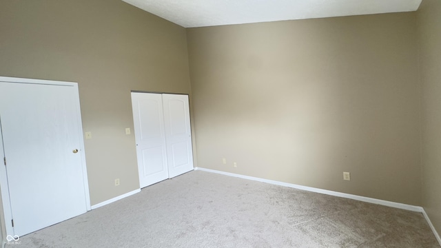 unfurnished bedroom with a high ceiling, a closet, carpet flooring, and baseboards