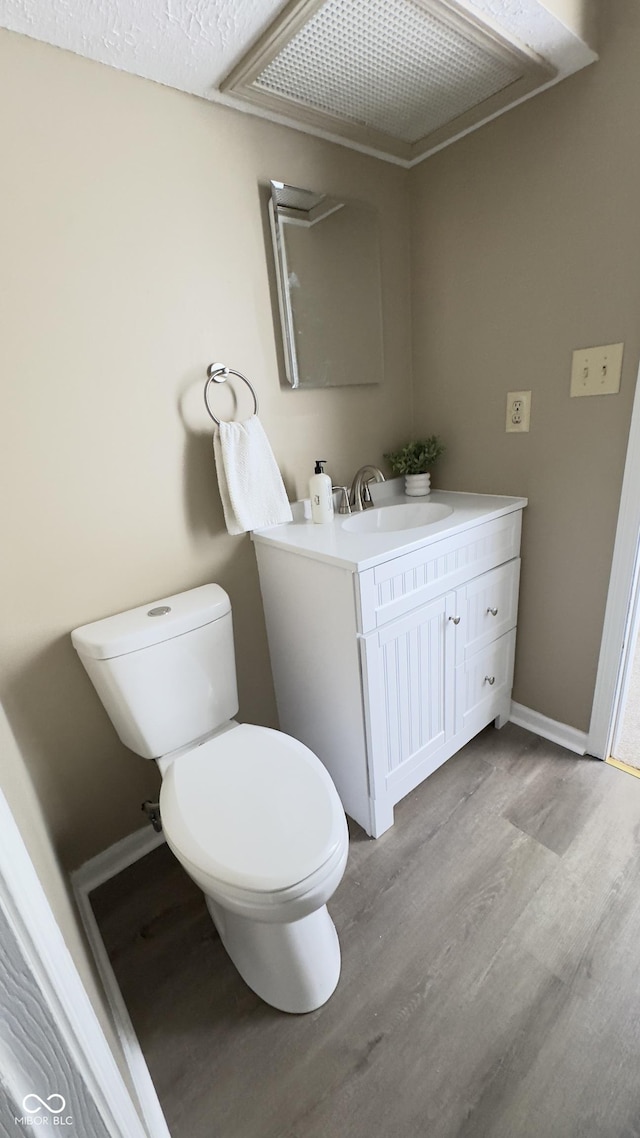 bathroom with a textured ceiling, toilet, wood finished floors, vanity, and baseboards