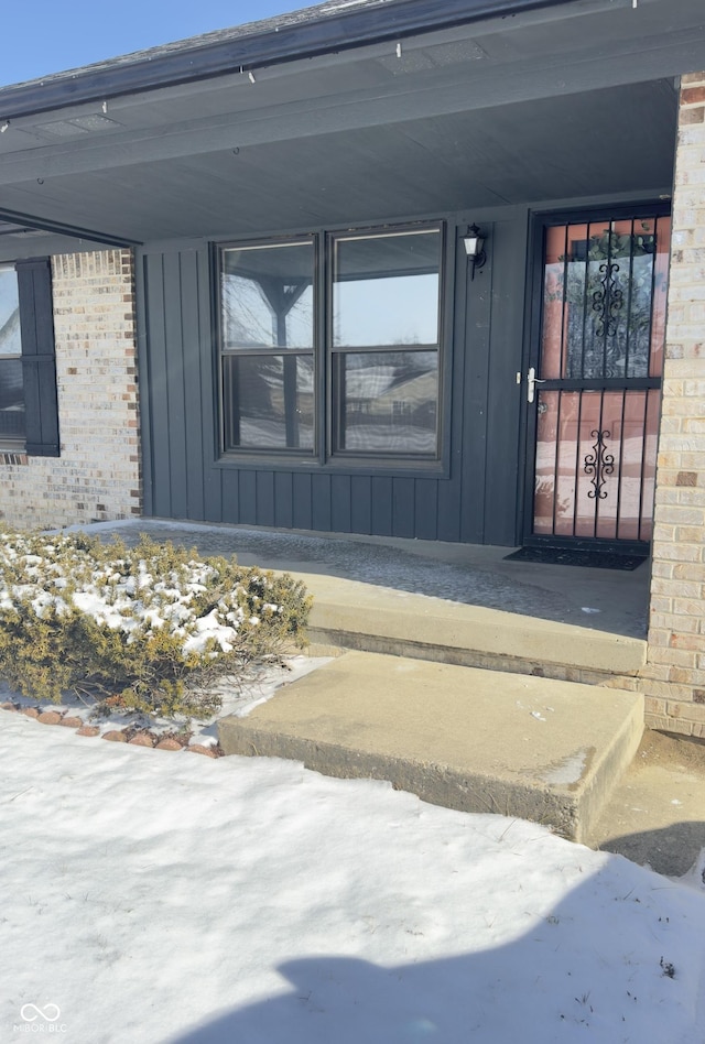 snow covered property entrance featuring brick siding and board and batten siding