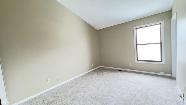 spare room with visible vents, baseboards, vaulted ceiling, and light colored carpet