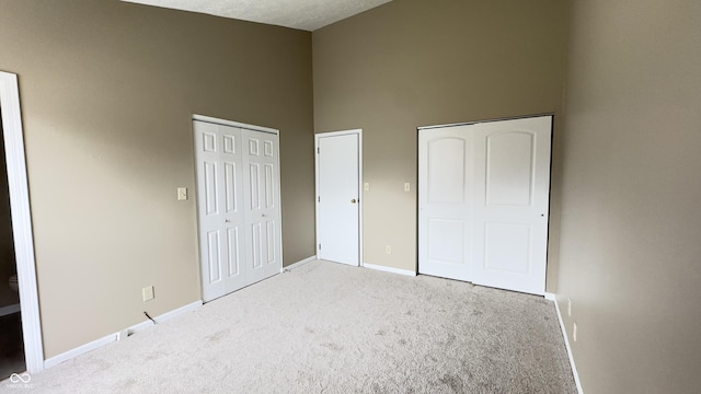 unfurnished bedroom featuring high vaulted ceiling, light carpet, baseboards, and two closets