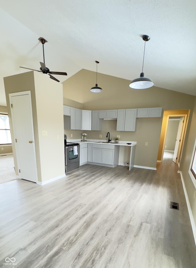 kitchen featuring decorative light fixtures, stainless steel electric stove, vaulted ceiling, light countertops, and a sink