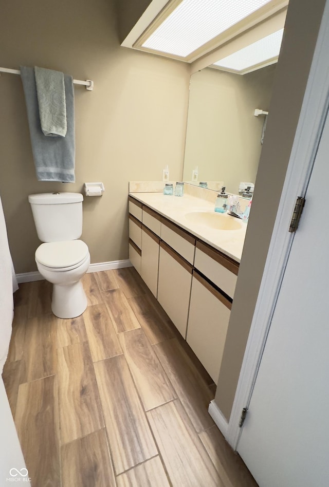 half bathroom with toilet, baseboards, wood finished floors, and vanity