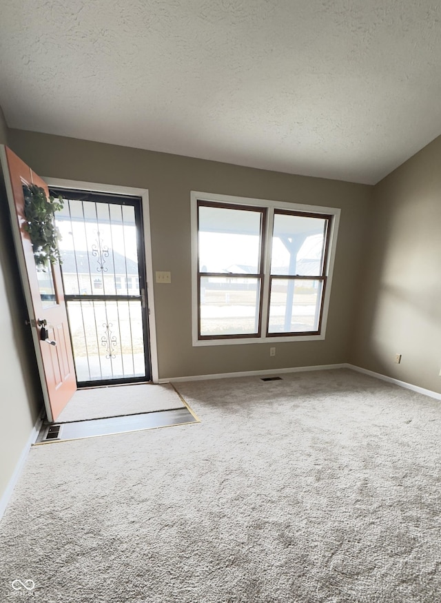 entryway with baseboards, a textured ceiling, visible vents, and carpet flooring