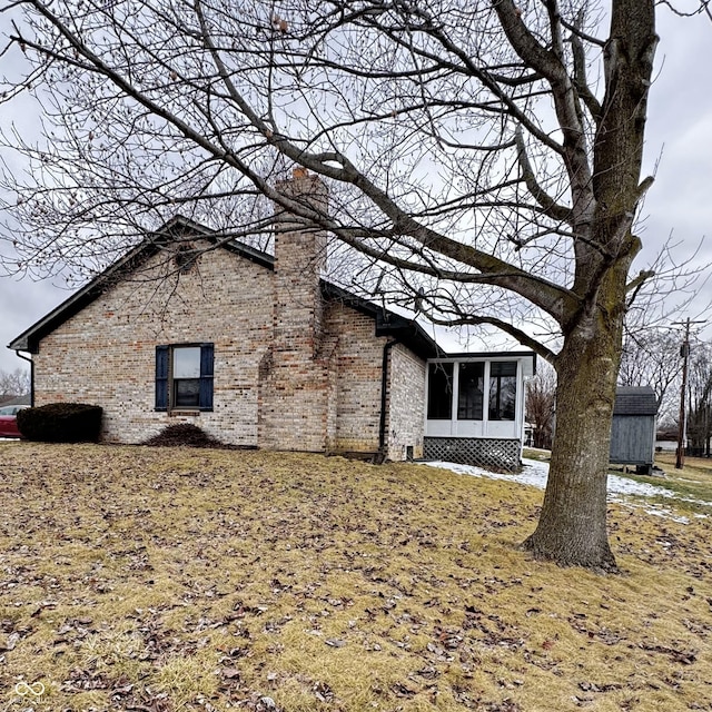 exterior space with brick siding, a chimney, and a sunroom