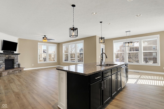 kitchen featuring a fireplace, stainless steel dishwasher, a sink, dark cabinets, and light wood-type flooring