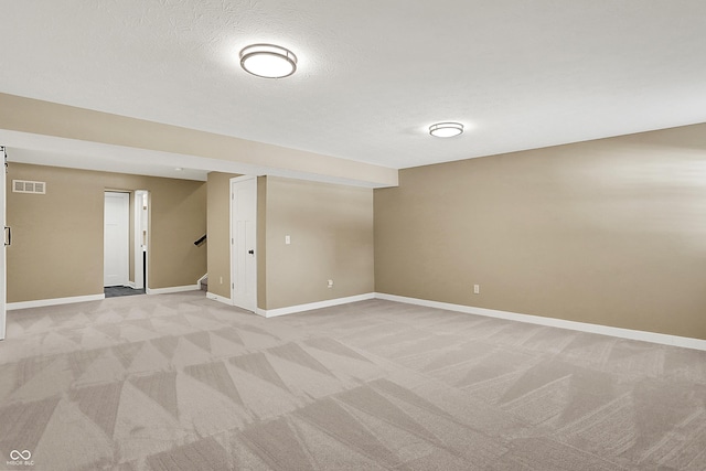 finished below grade area with light carpet, stairway, baseboards, and a textured ceiling