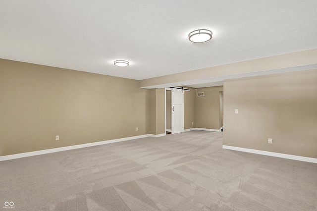 unfurnished room featuring a barn door, baseboards, a textured ceiling, and light colored carpet