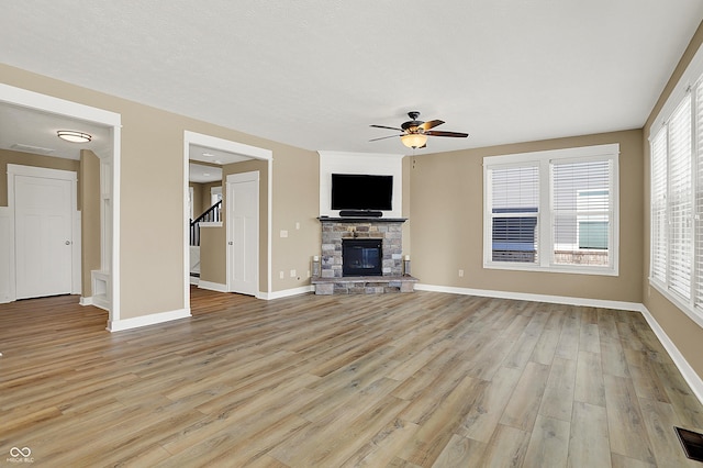 unfurnished living room featuring baseboards, a ceiling fan, light wood-style flooring, stairs, and a fireplace