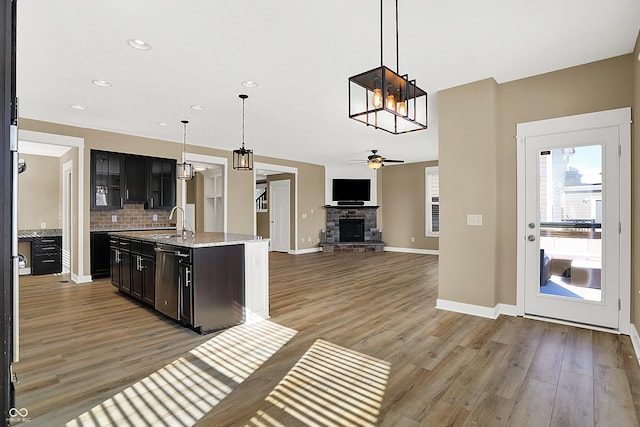 kitchen featuring a fireplace, tasteful backsplash, hanging light fixtures, light wood-style flooring, and a ceiling fan