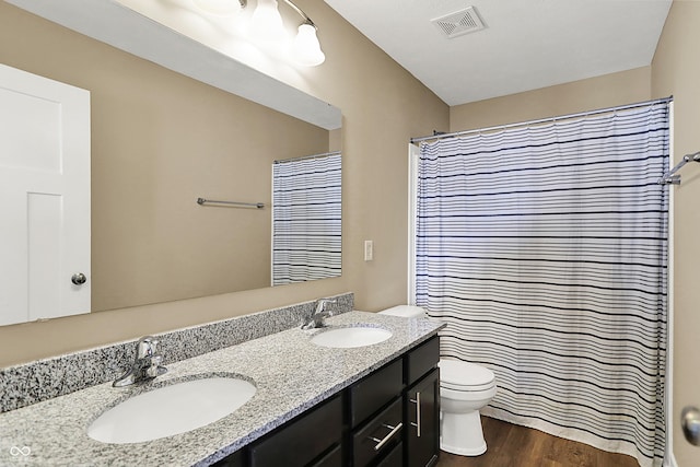 full bath with toilet, double vanity, a sink, and wood finished floors