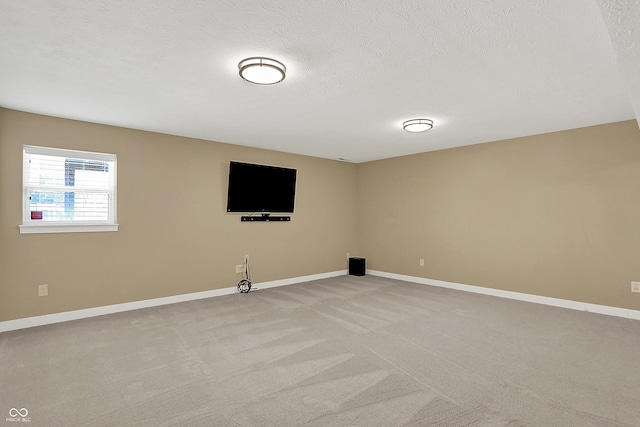 spare room featuring light carpet, baseboards, and a textured ceiling