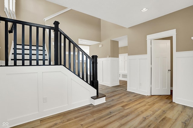 stairway with recessed lighting, wainscoting, wood finished floors, and a decorative wall